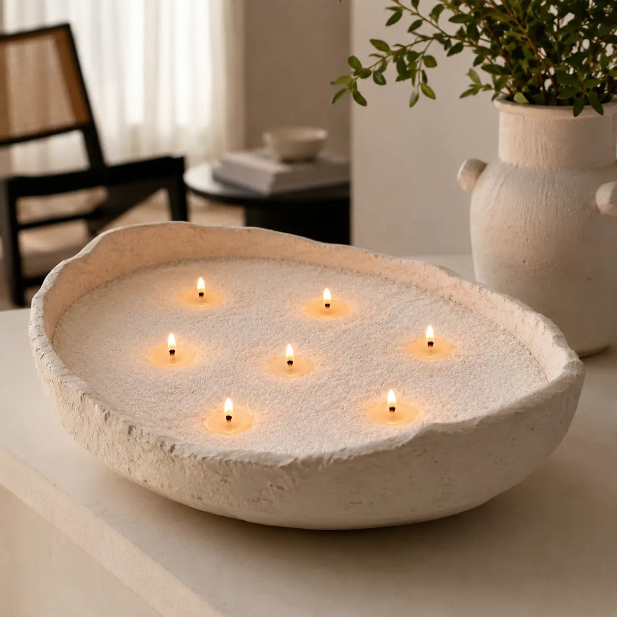 Large off-white handcrafted bowl filled with soft white pearled candle wax and seven lit wicks, styled in a warm minimalist interior for Luster Candle