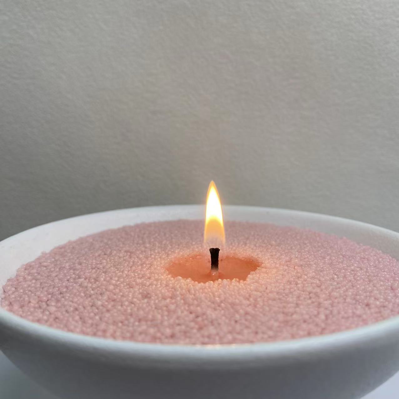 Close-up of Blush Rose scented pearled candle wax with a warm candle flame and realistic melted wax around the wick.