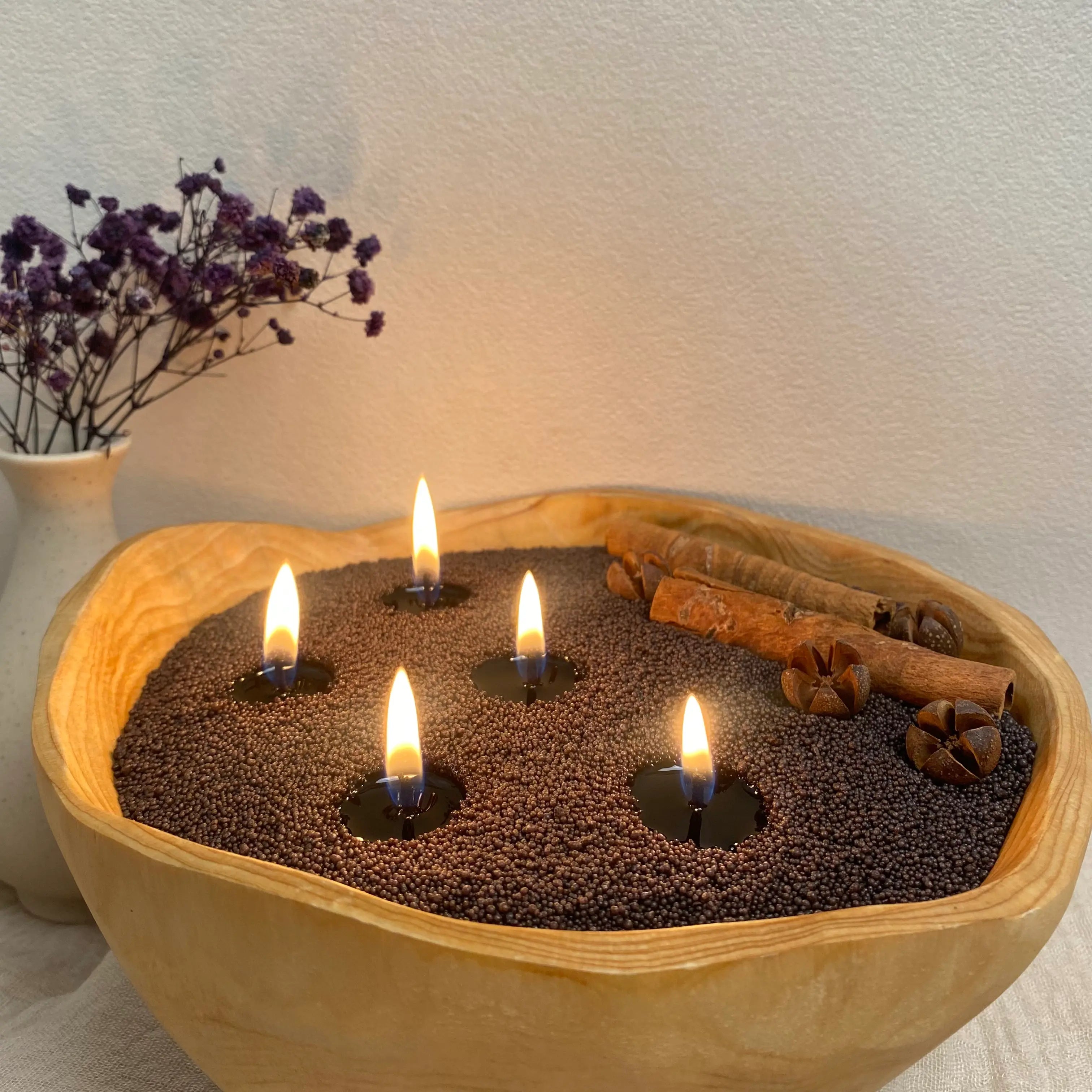 Charcoal Black pearled candle wax in a wooden candle bowl with soft flames, cinnamon decor, and dried flowers.