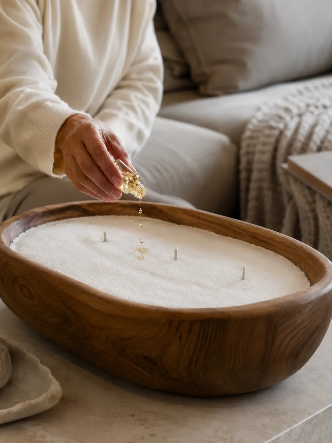 Adding fragrance oil to soft white pearled candle wax before lighting, with unlit wicks in a wooden vessel for safe scented candle styling