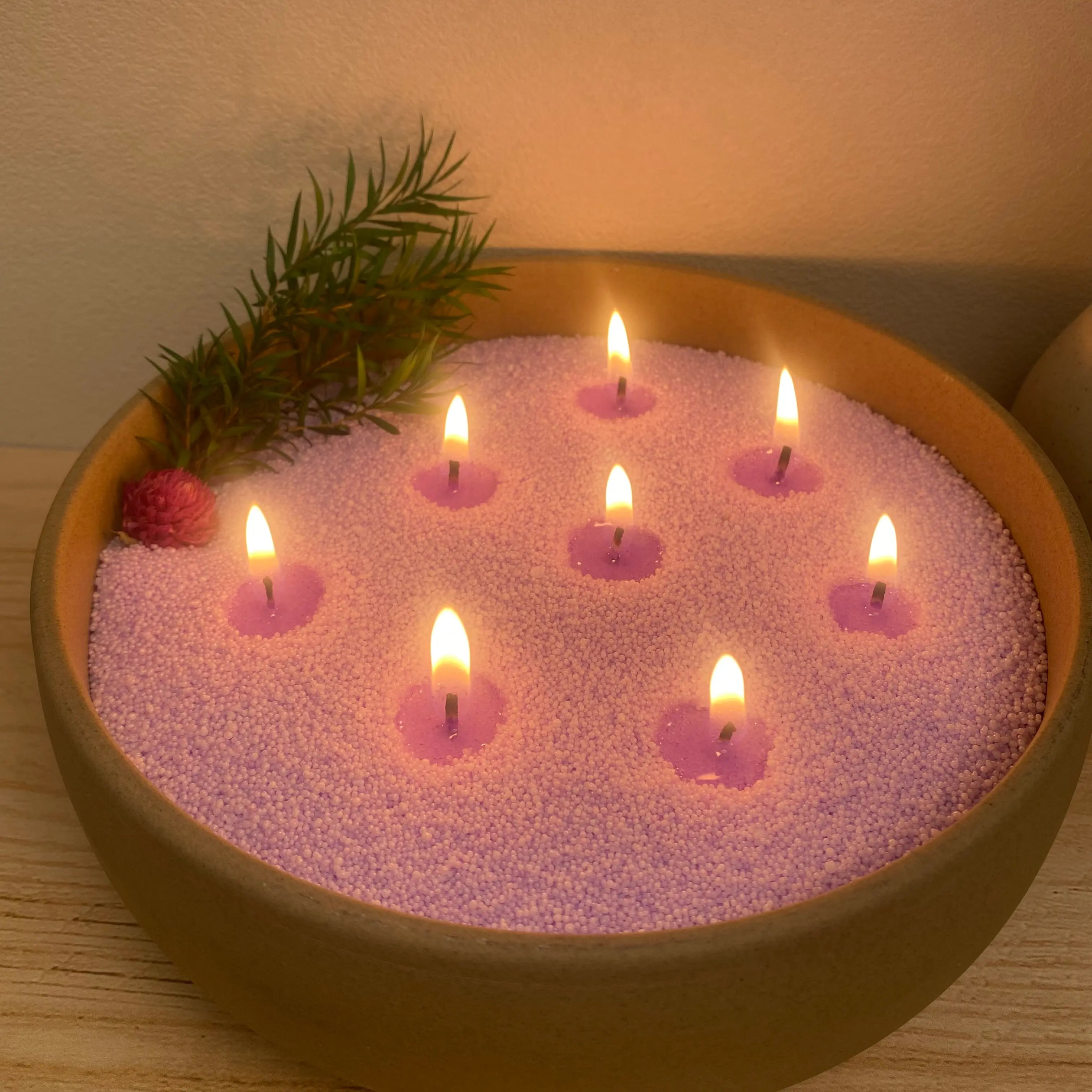 Lavender Purple pearled candle wax in a wooden bowl with multiple cotton wicks, warm flames, and dried floral decor.
