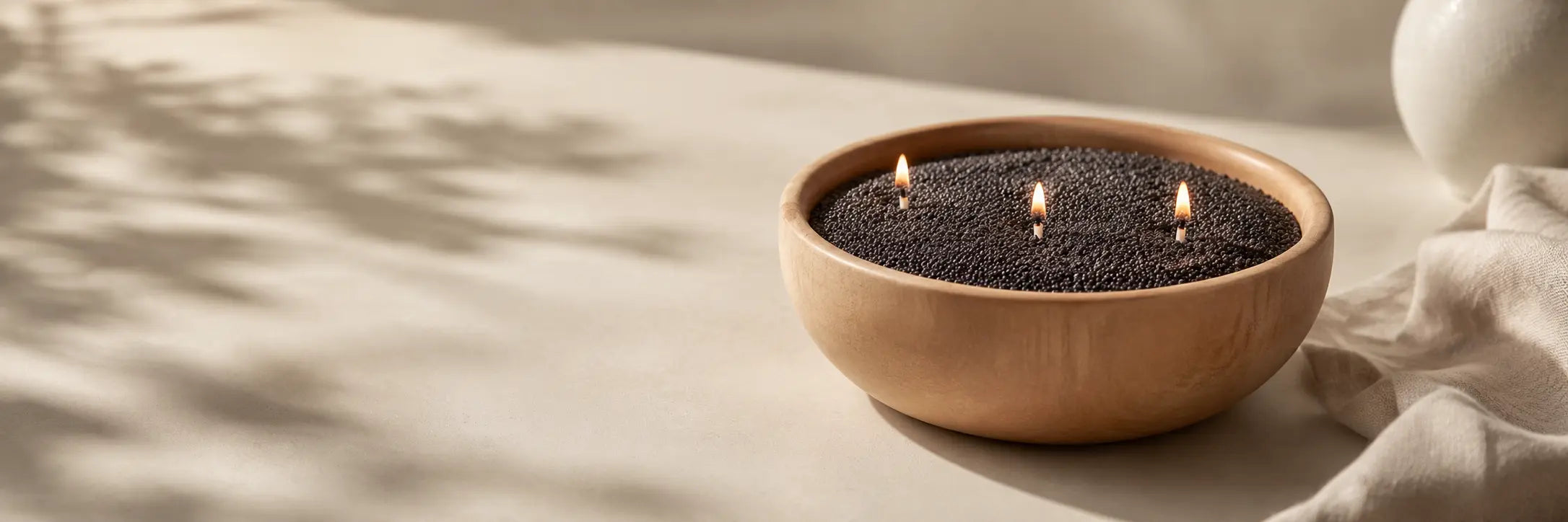 Black pearled candle wax in a smooth wooden bowl with lit wicks on a warm beige Scandinavian-style blog banner.