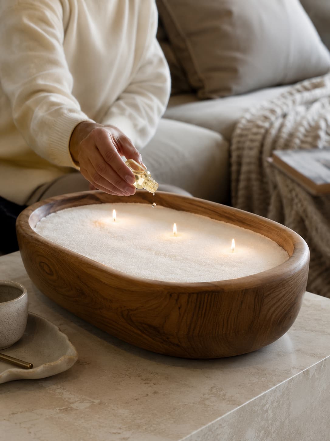 soft white pearled candle wax in a large wooden vessel with fragrance oil being added in a cozy modern home setting.