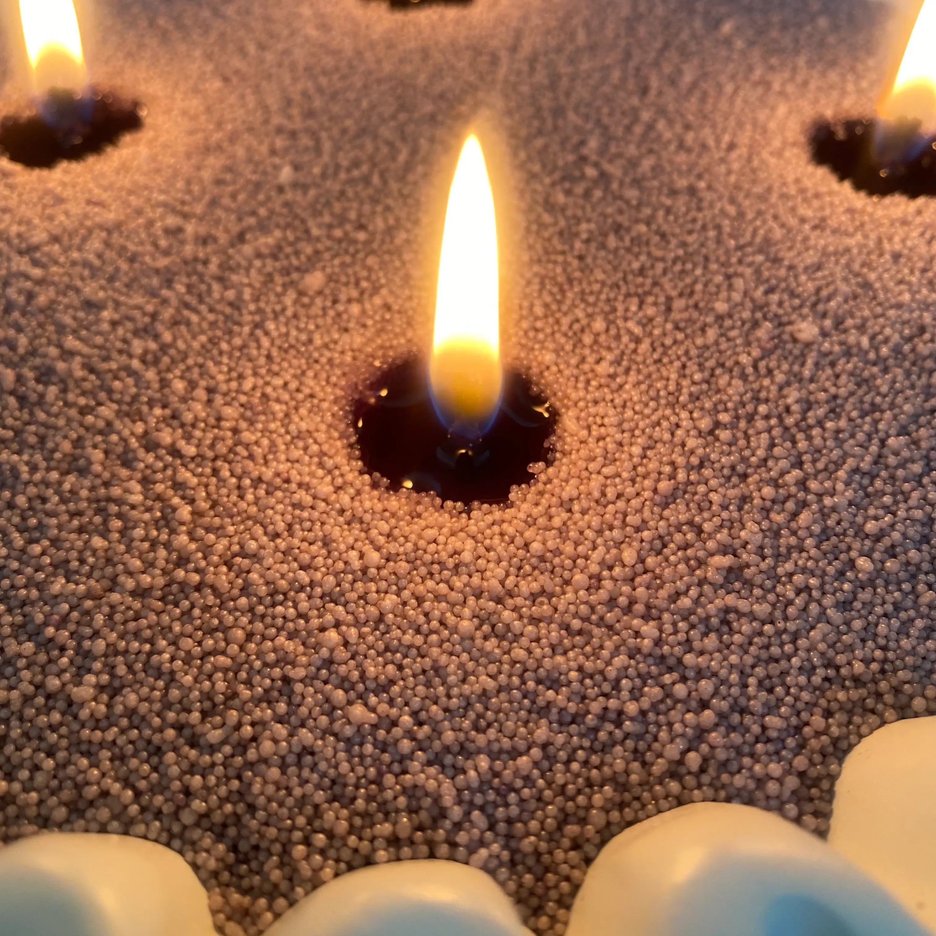 Mist Grey pearled candle wax close-up showing realistic wax beads, a cotton wick, and a warm candle flame.