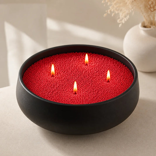 Red pearled candle wax in a black bowl with four lit wicks