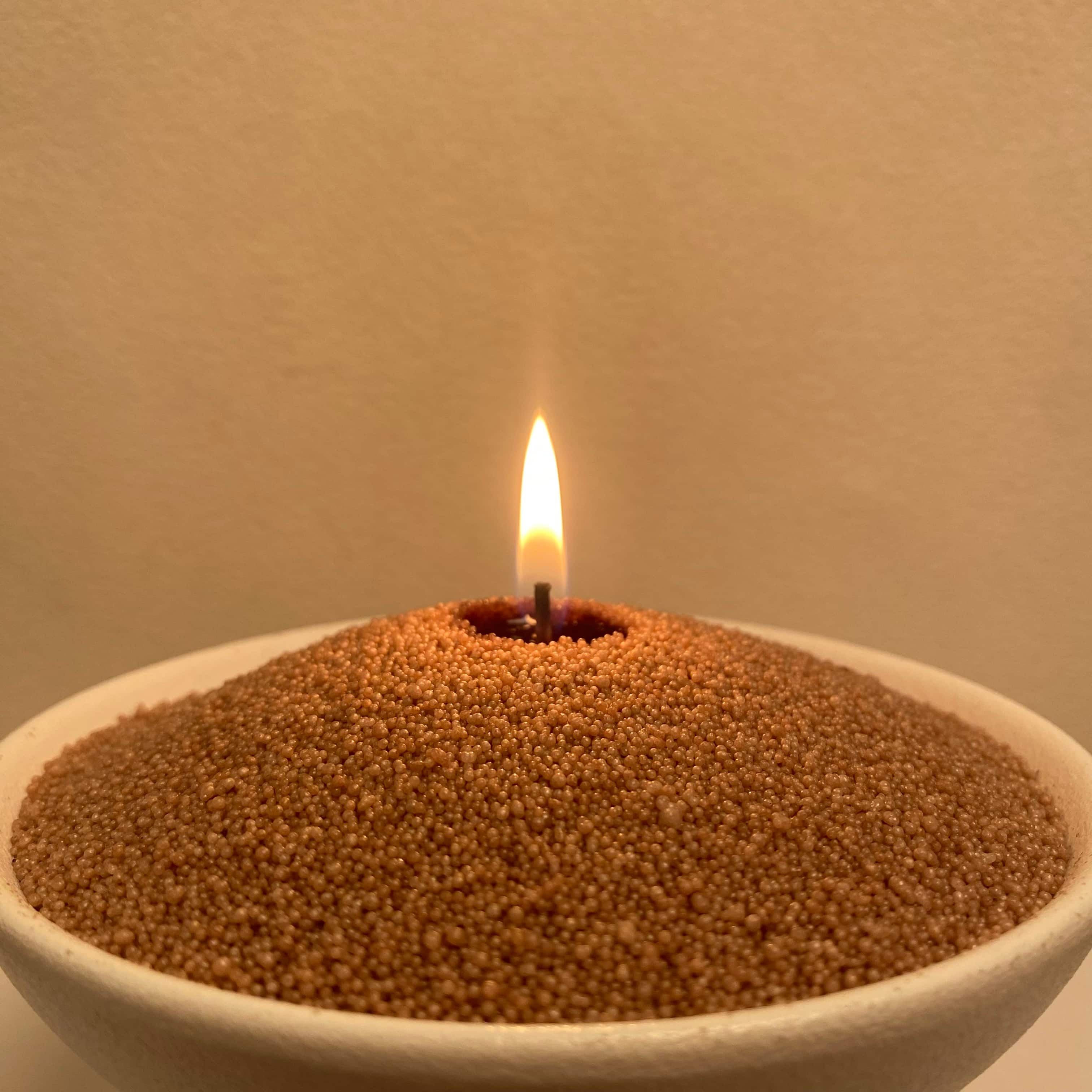 Close-up of warm taupe pearled candle wax beads with a single cotton wick and soft flame.