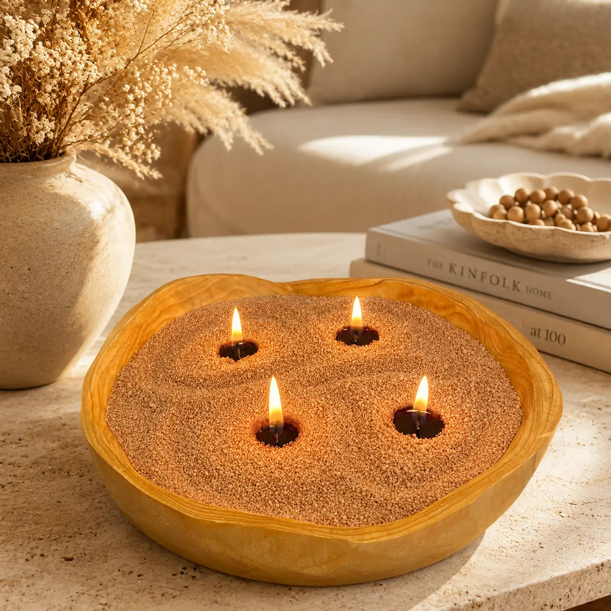 Warm taupe pearled candle wax in a wooden candle bowl with soft flames on a beige stone coffee table in a warm living room.