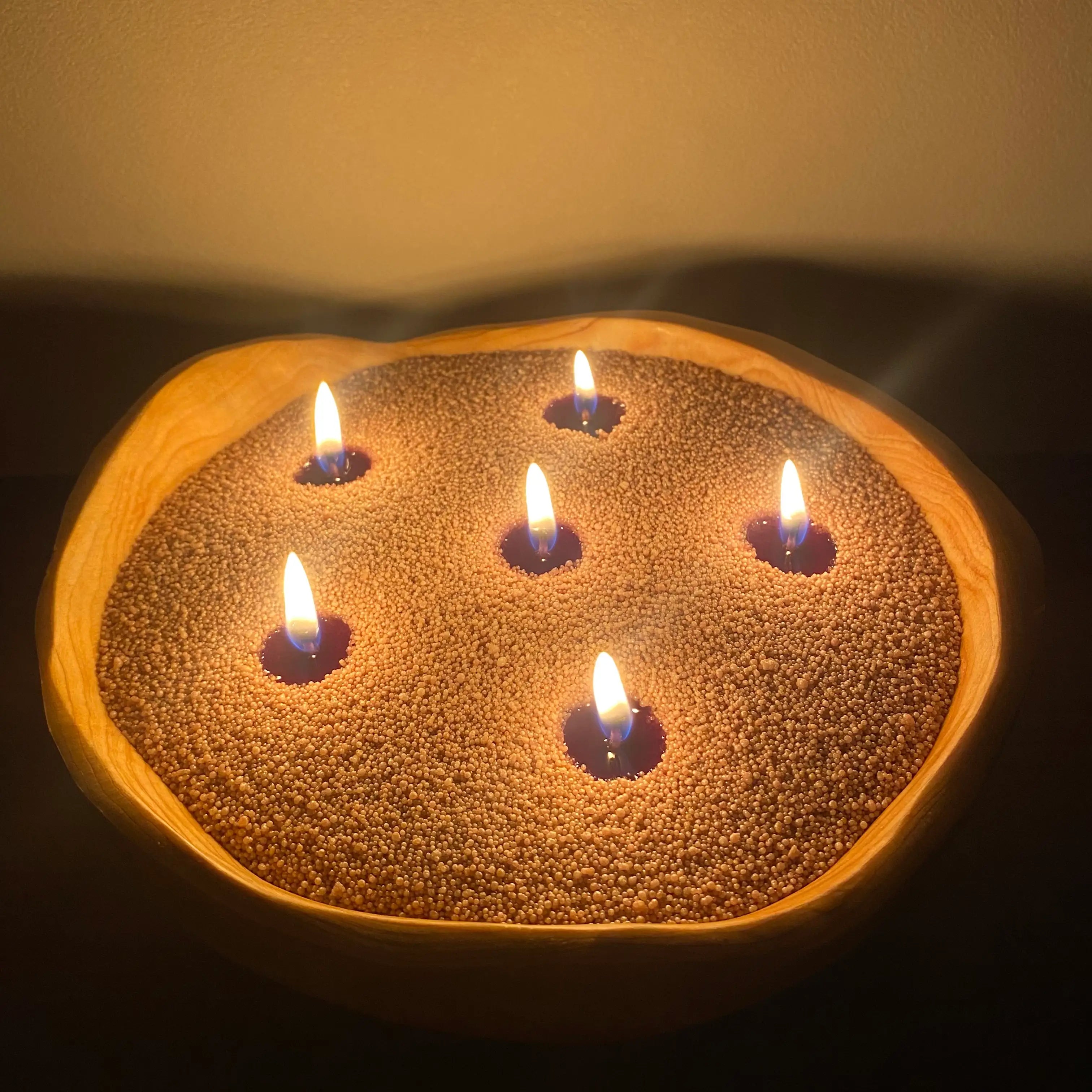 Warm taupe pearled candle wax in a wooden candle bowl with multiple cotton wicks and soft flames.